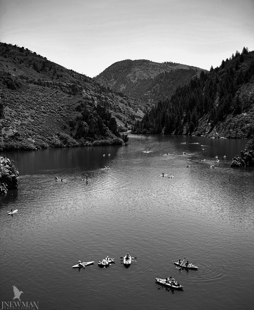 Black and white view of a lake surrounded by mountains, with boats and people enjoying the water.