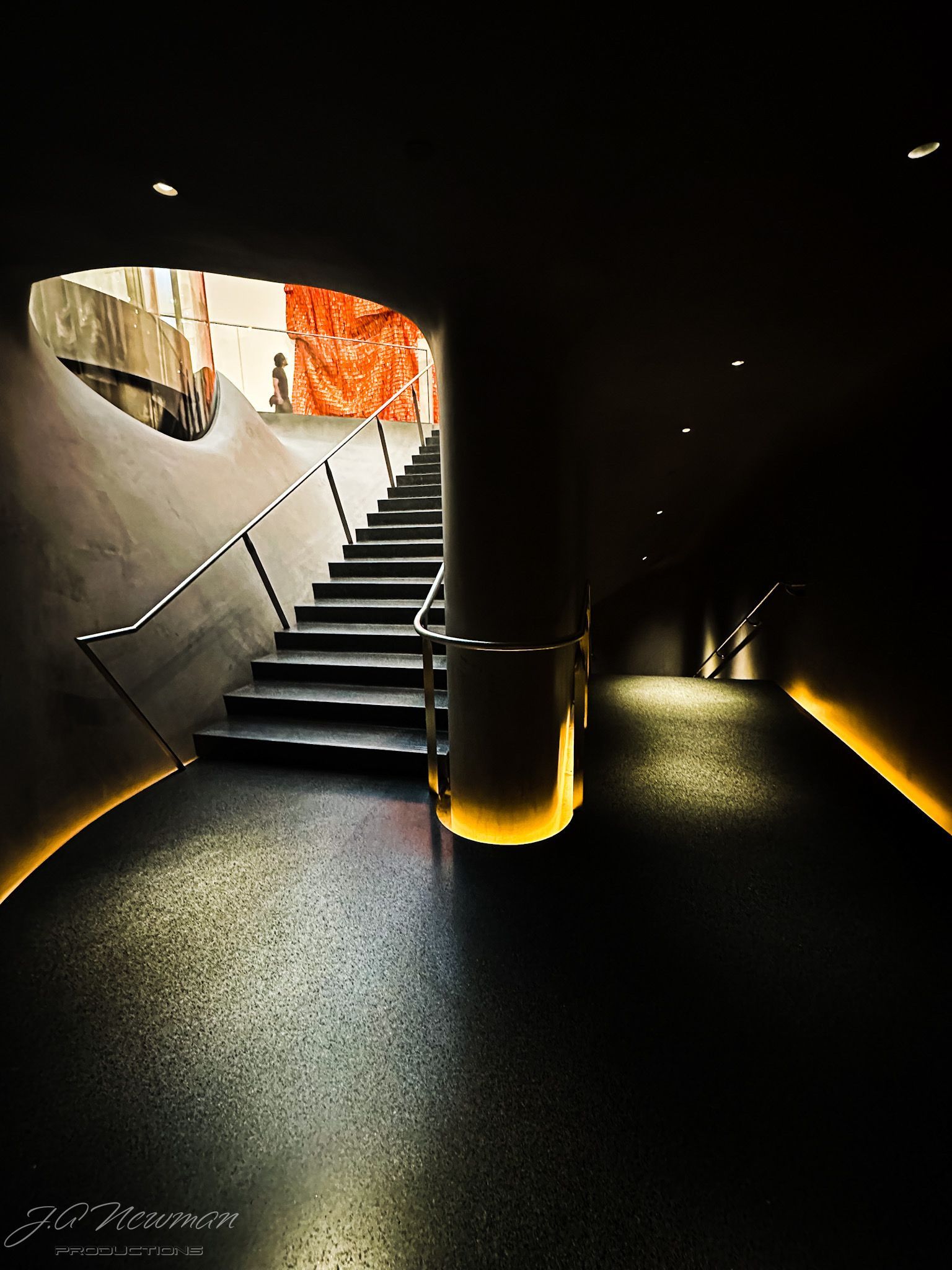 Dark, modern interior with stairs and a hallway. Warm lighting illuminates the path.
