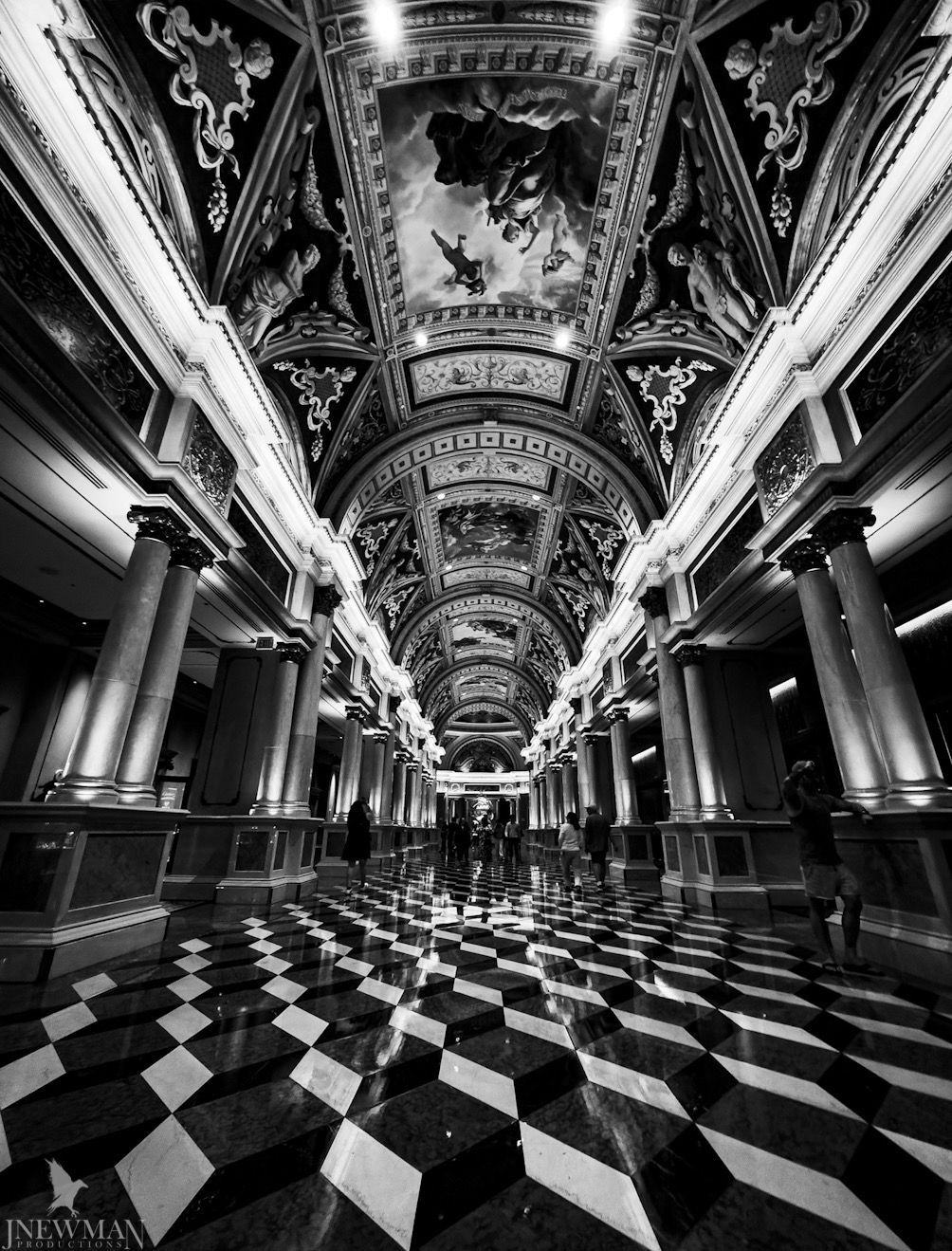 Black and white perspective of a long, ornate hallway with checkered floor and painted ceiling.