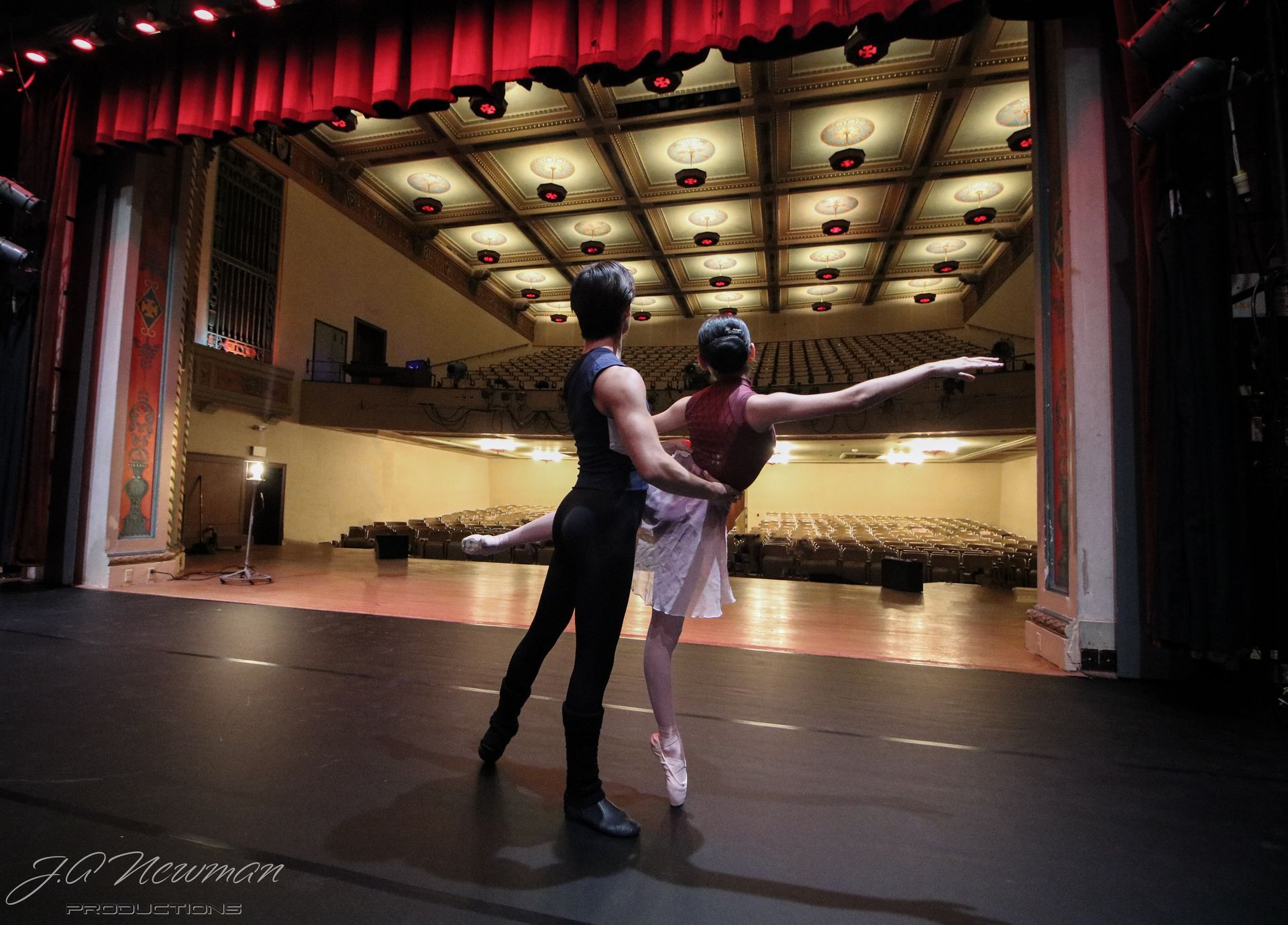 Ballet dancers on stage, man holding woman as she balances en pointe with outstretched arm; theater.