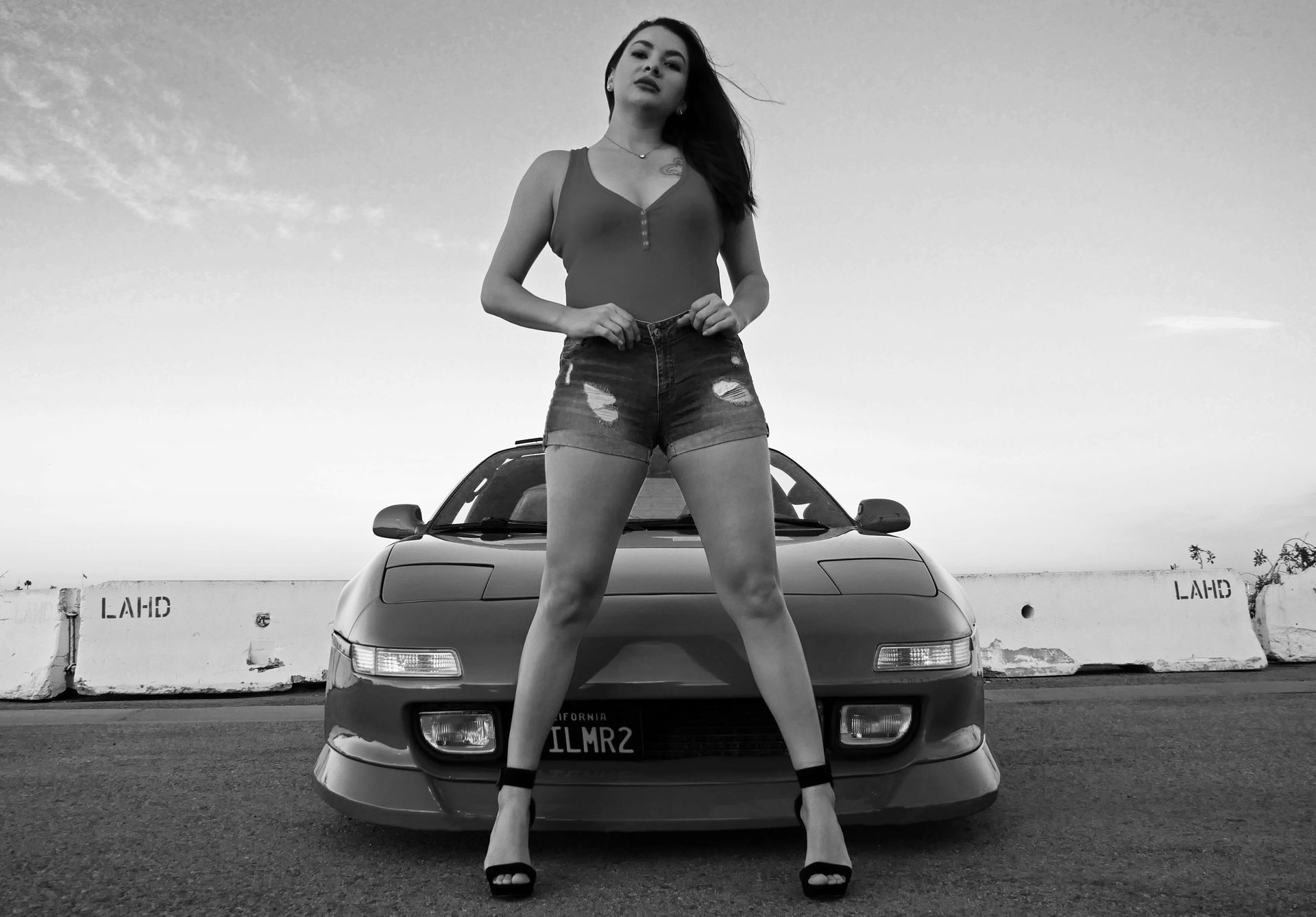 Woman in red top and denim shorts posing in front of a red sports car.