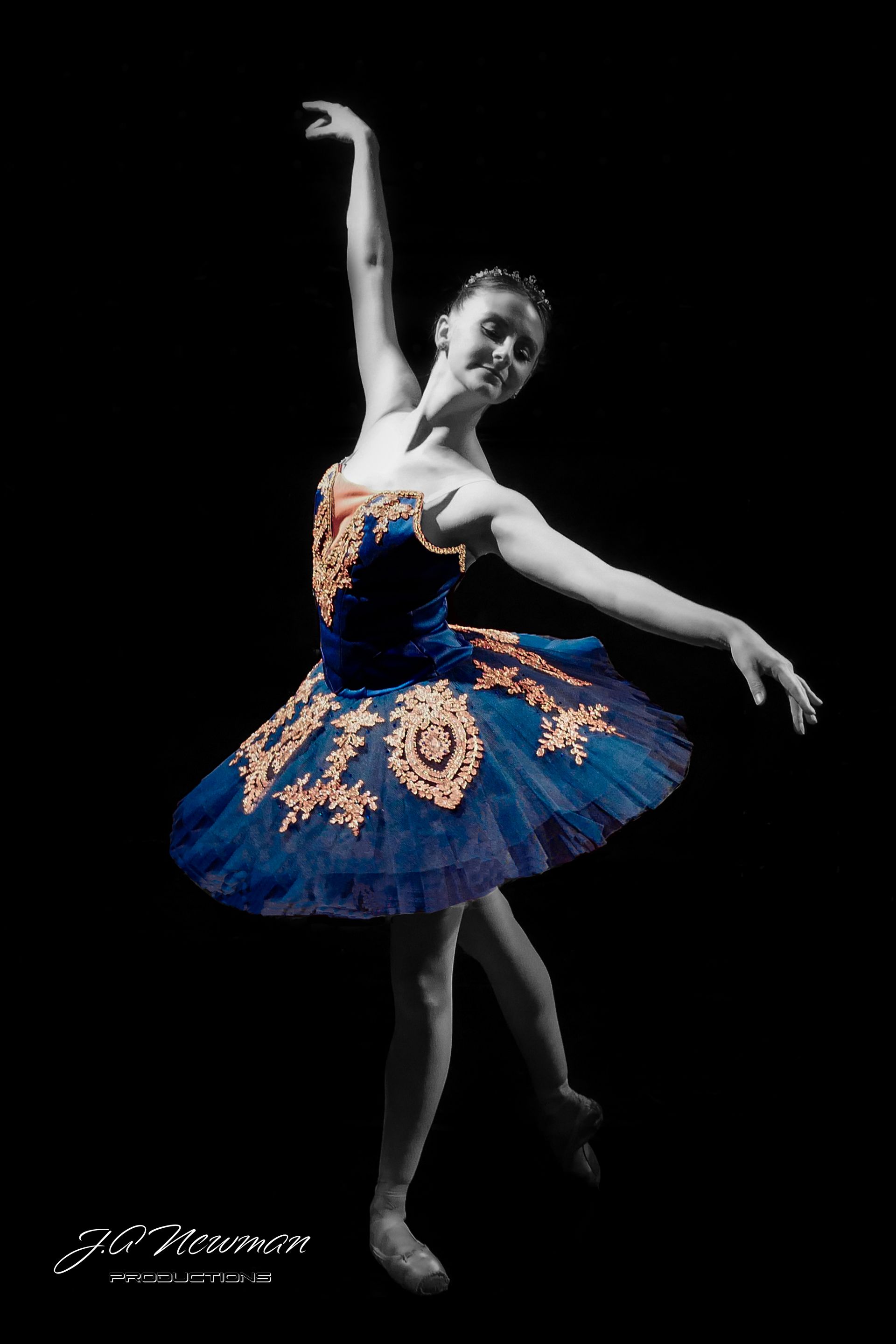 Ballerina in blue tutu, arms raised, poised en pointe. Black background, detailed costume.