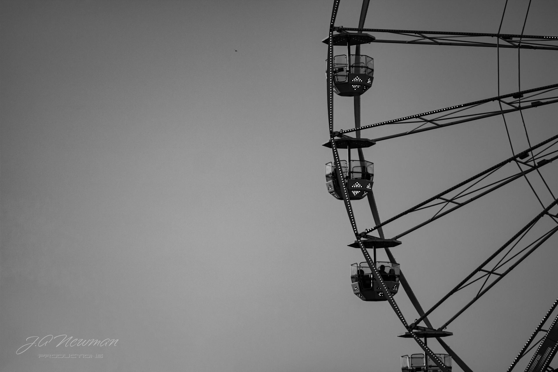 Black and white photo of a Ferris wheel against a clear sky, several gondolas with passengers.