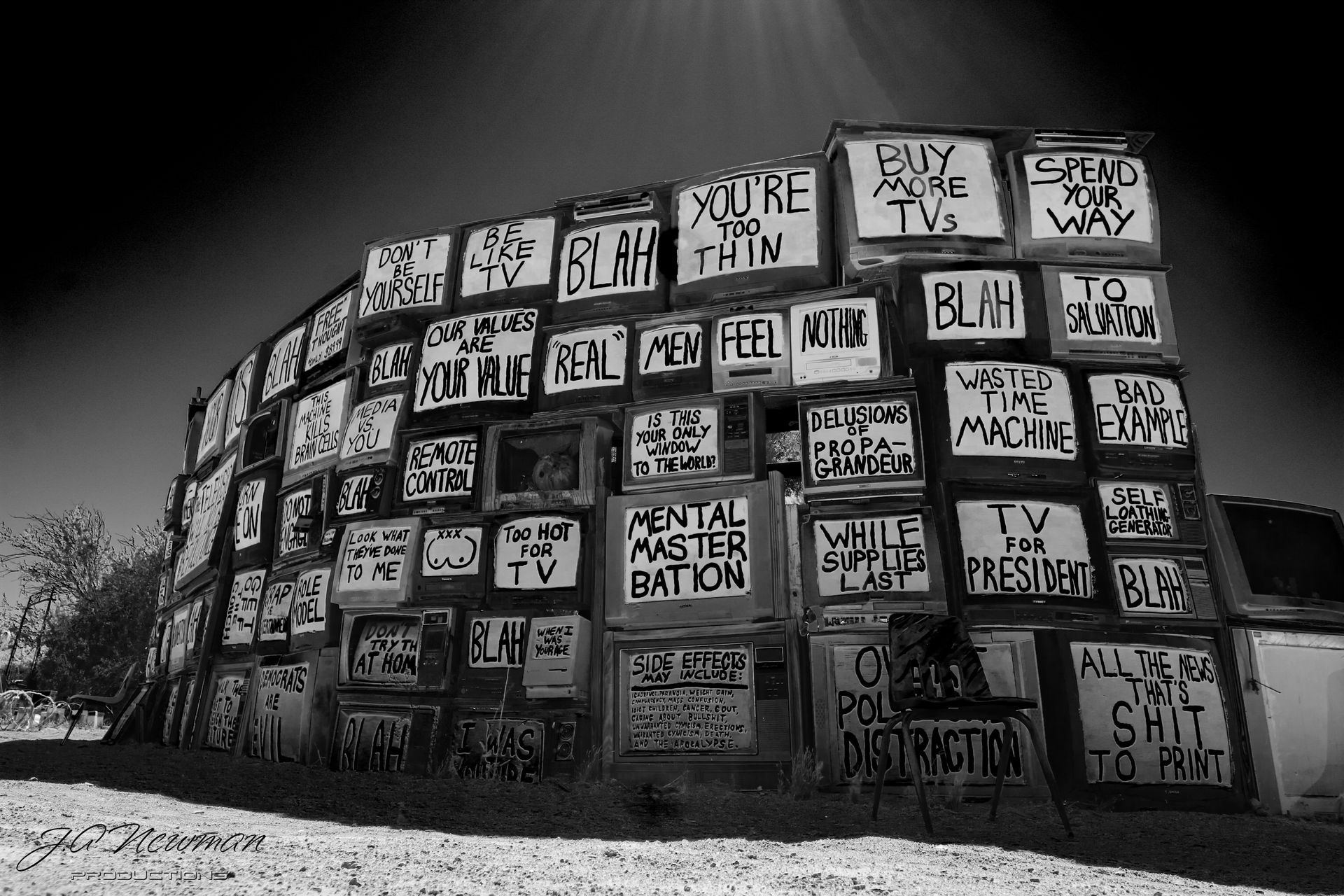 A building covered in old TV sets, spray-painted with phrases in black and white, set outdoors.
