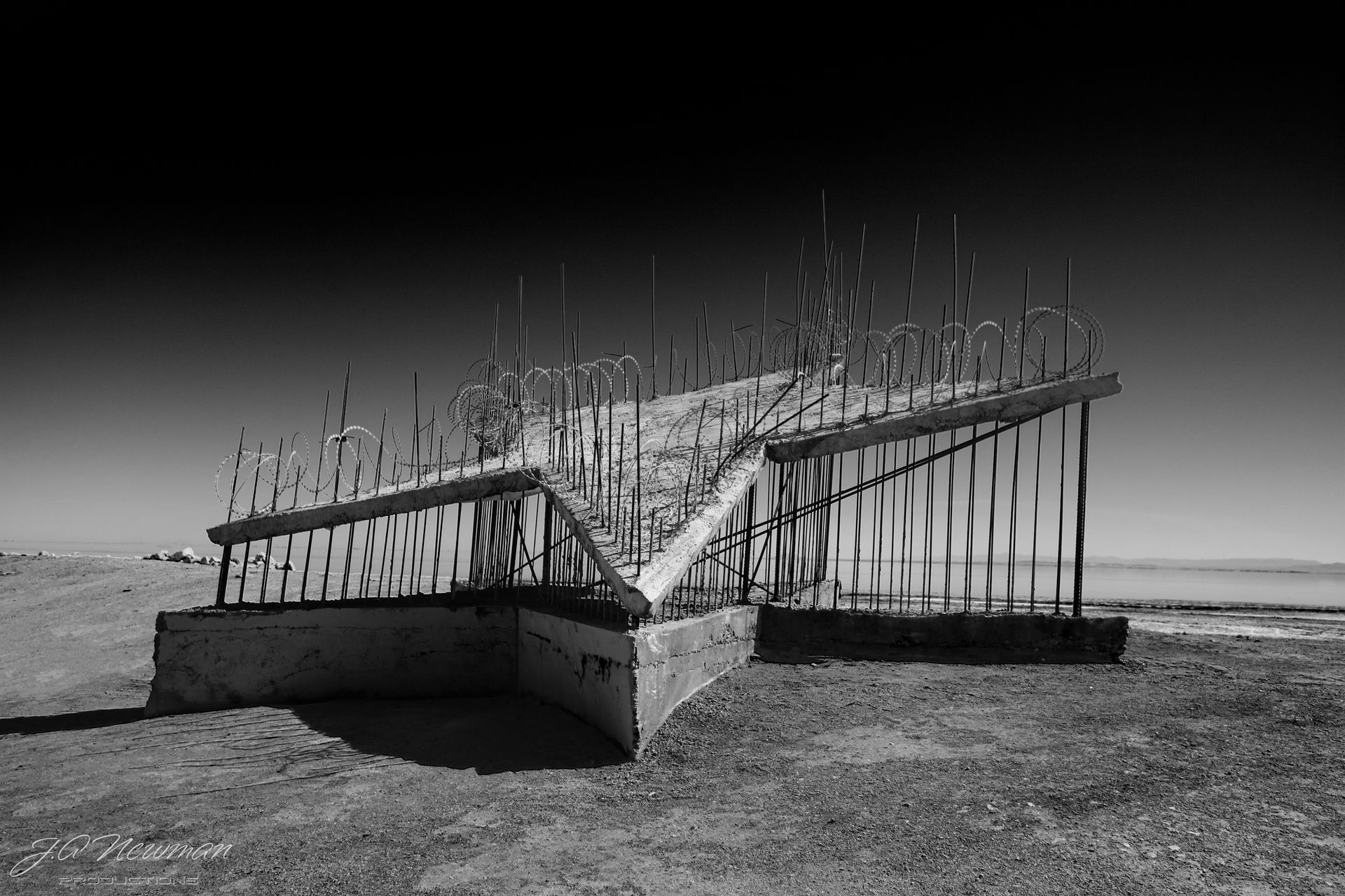 Black and white photograph of an abstract concrete and metal sculpture on a barren landscape, under a bright sky.