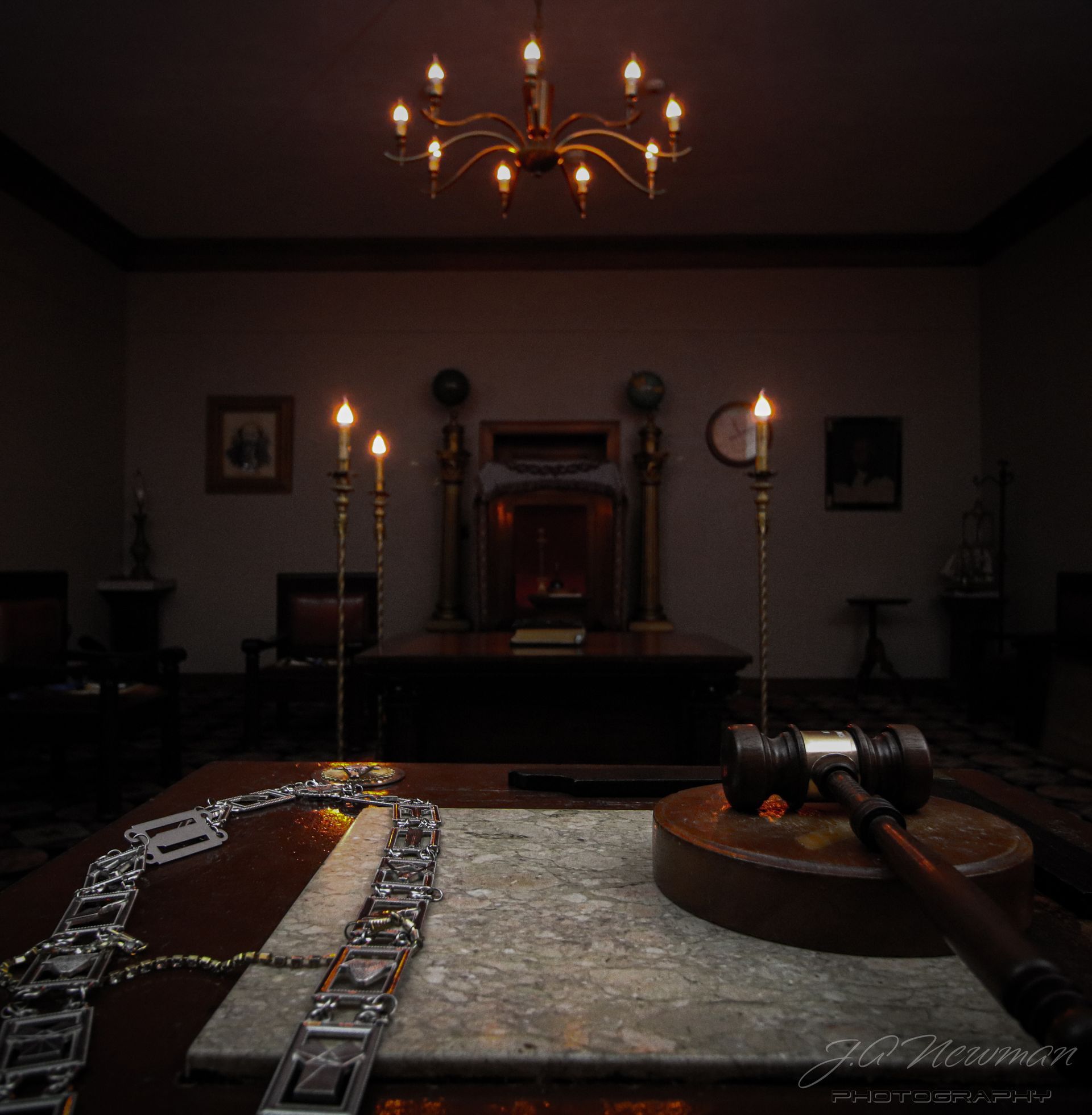 A dimly lit lodge room with a chandelier, gavel, chain, and a large desk.