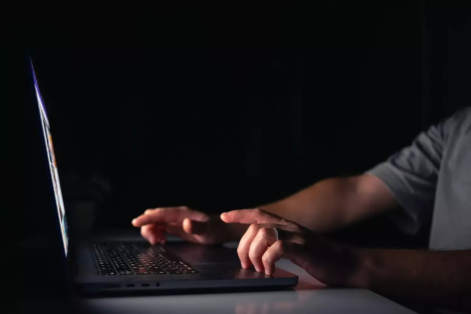 Uma pessoa está digitando em um laptop no escuro.