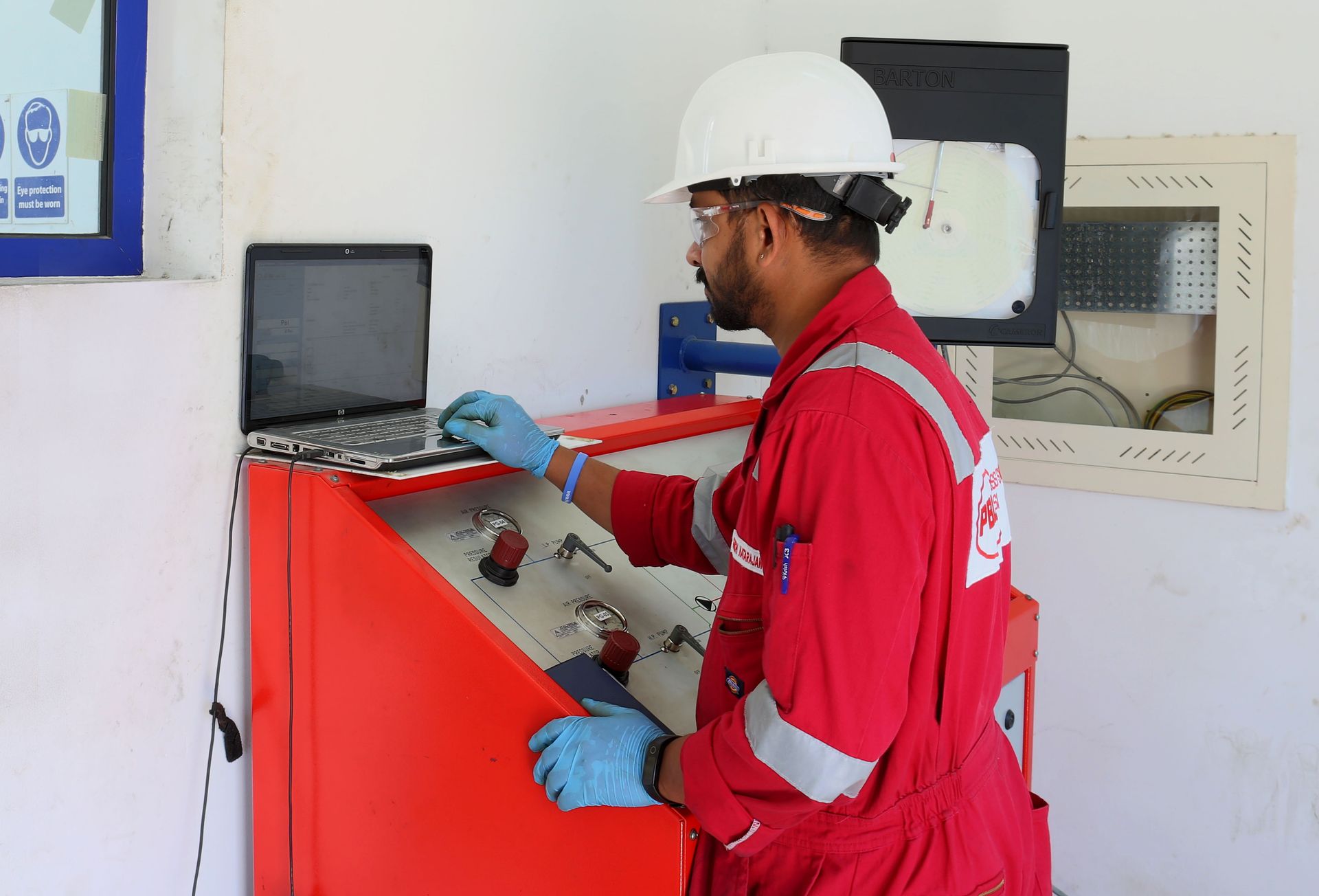 A man in a red jumpsuit is using a laptop computer.