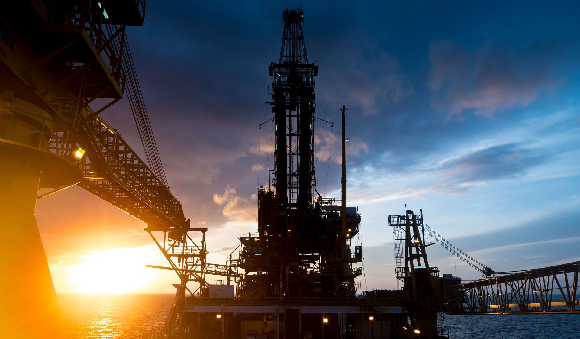 A large oil rig in the middle of the ocean at sunset.