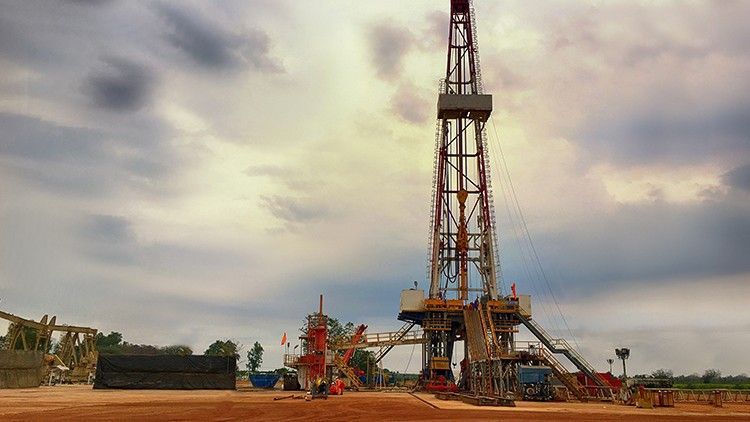 A large oil rig is sitting in the middle of desert with cloudy skies