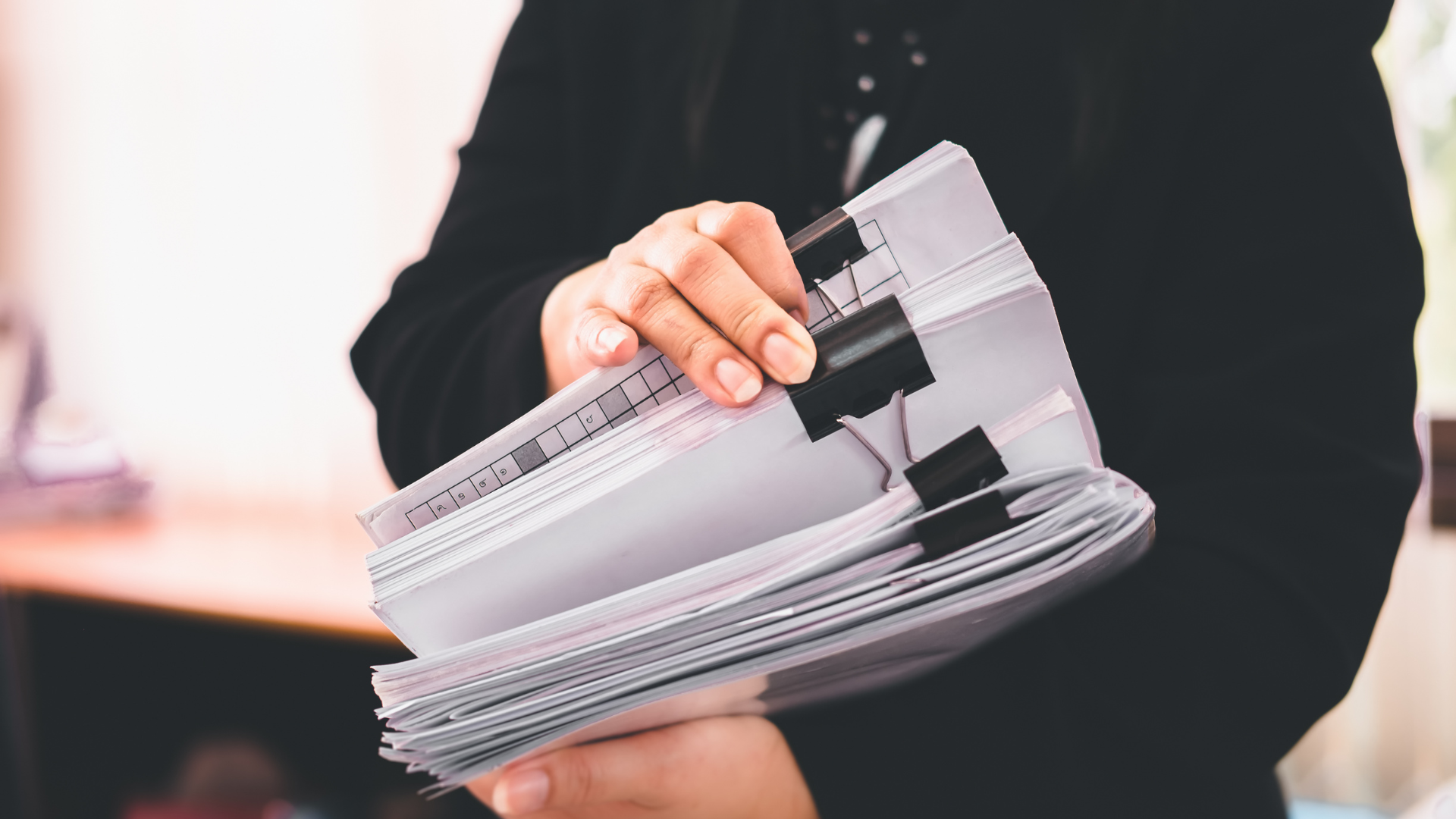 Person in black shirt holding a stack of papers held together by binder clips.