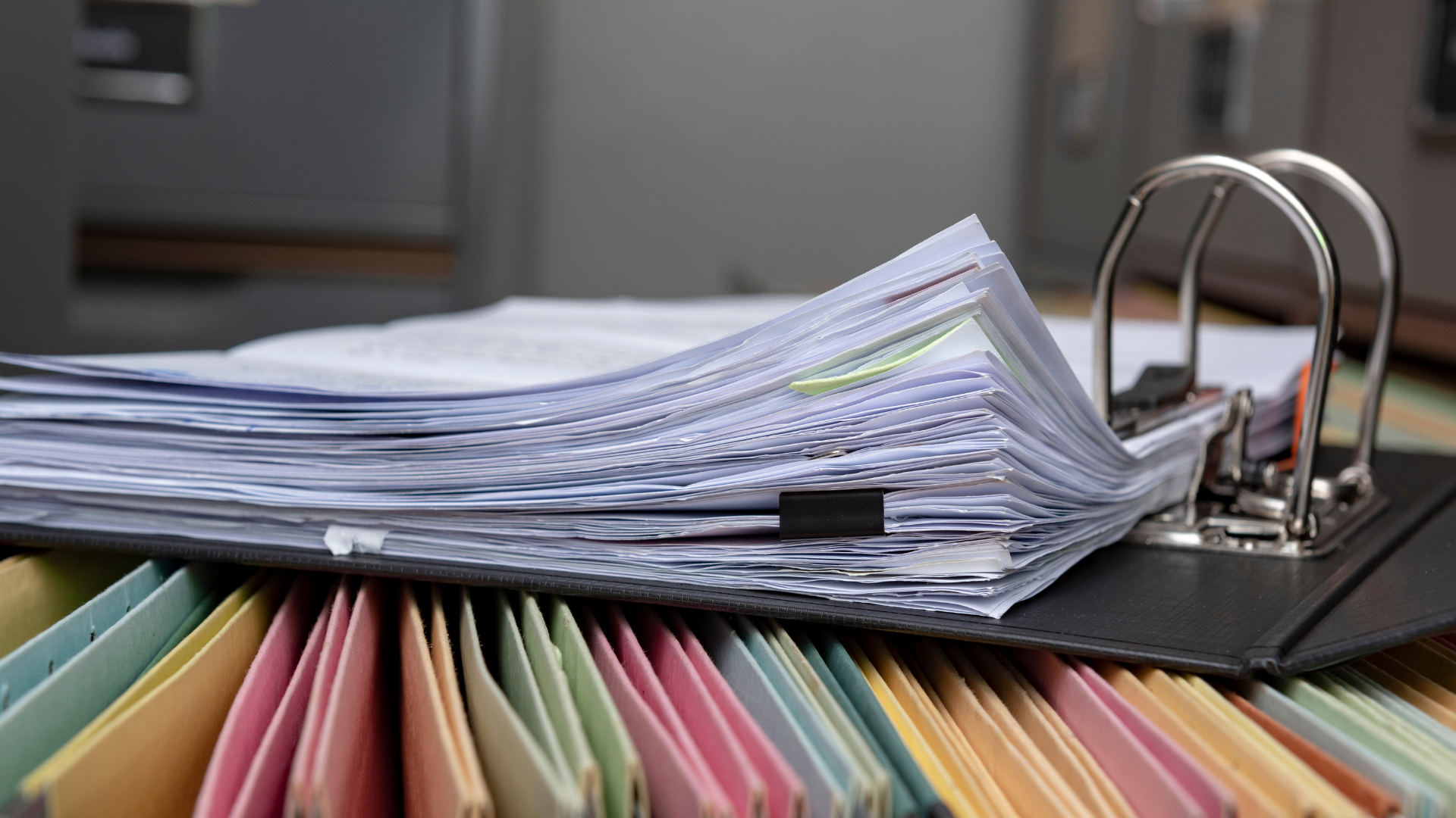 Binder with papers, open over color-coded file folders, in an office.