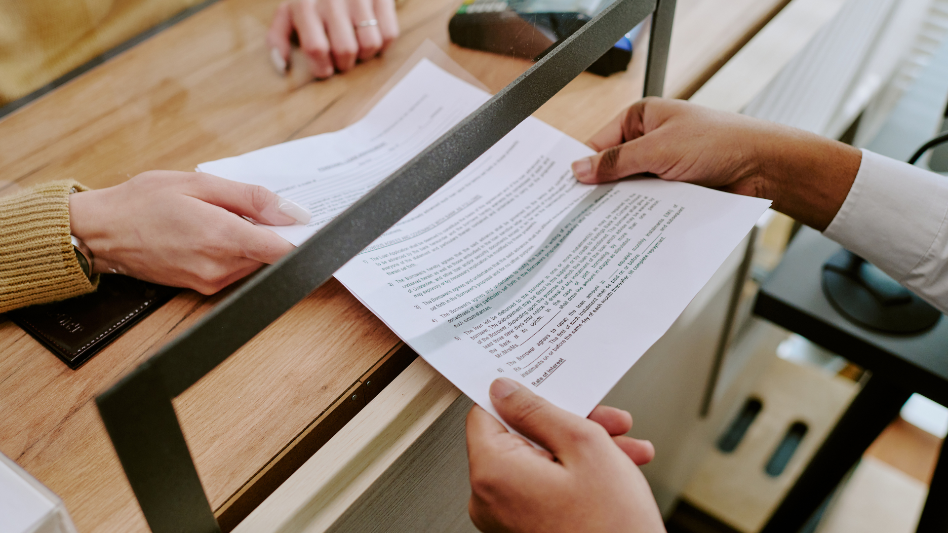 Hands exchanging documents at a counter, possibly a transaction or signing process.