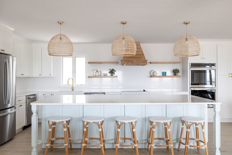 A kitchen with white cabinets , stainless steel appliances , a large island , and wicker stools.