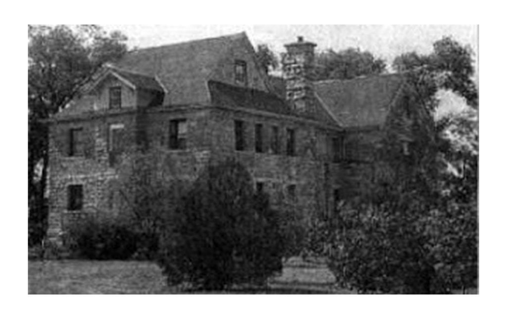 Stone building with multiple stories and a chimney, surrounded by trees.