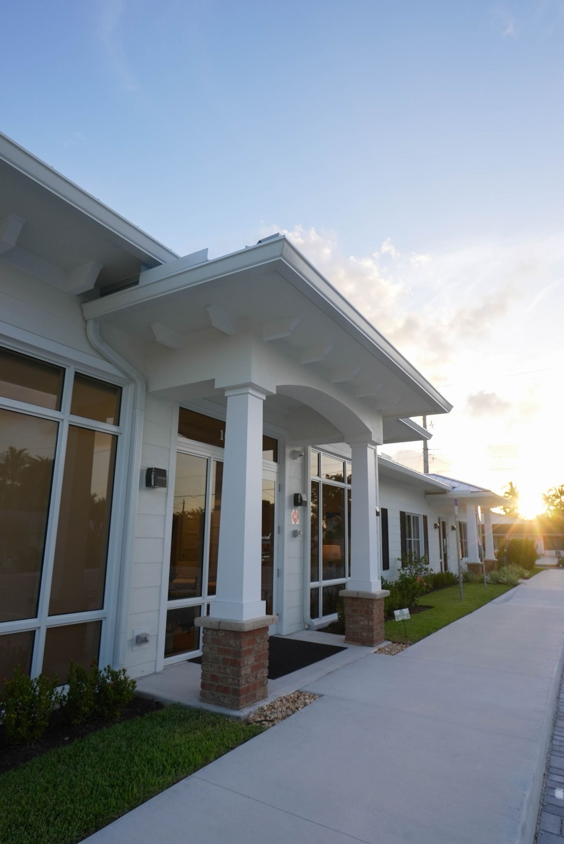 White building with large windows, brick columns, and covered entrance. Exterior shot.