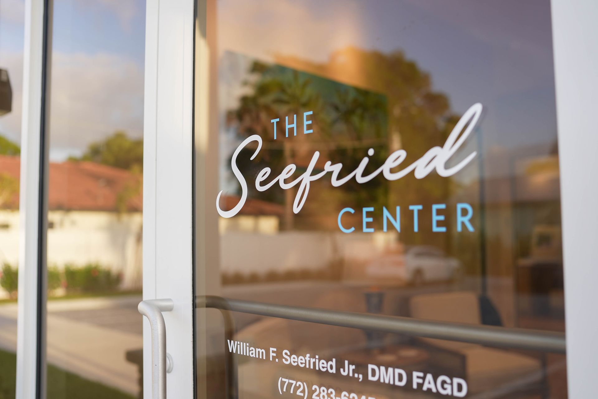 The Seefried Center entrance door with white lettering. Reflects building, car, trees.