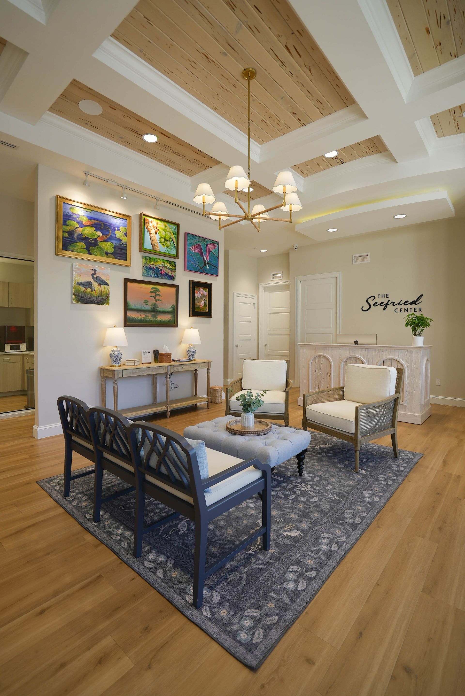 Waiting area with artwork, chairs, rug, and a reception desk, light wood ceiling.