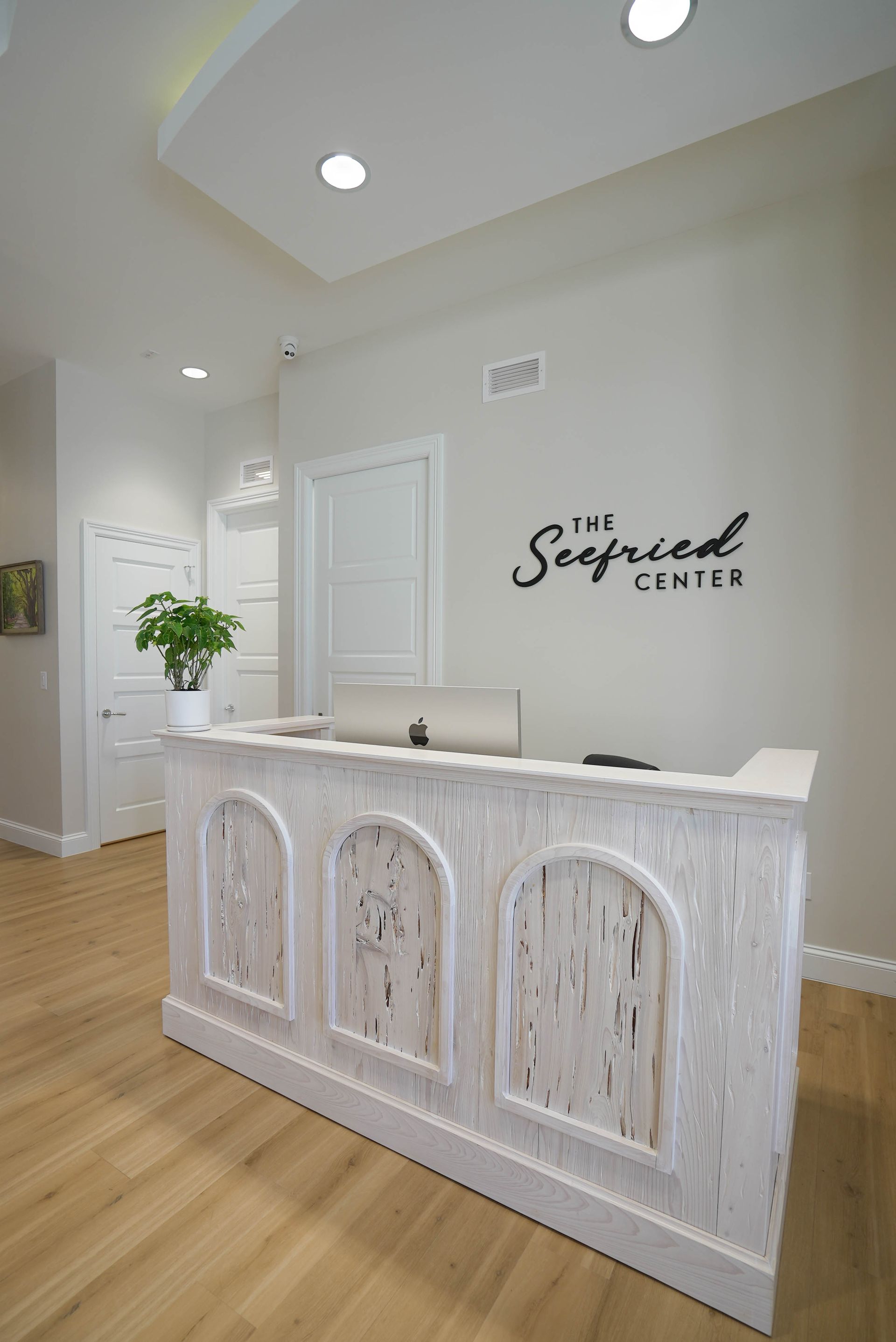 Reception desk with weathered white finish in a neutral-toned medical office. The Seefried Center logo is visible.