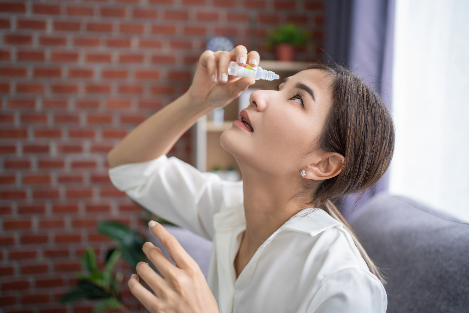 Young woman using eye drops to relieve dry eyes disease, a primary symptom of autoimmune Sjögren's