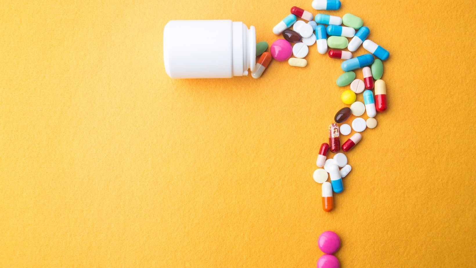 Colorful pills forming a question mark shape on an orange background