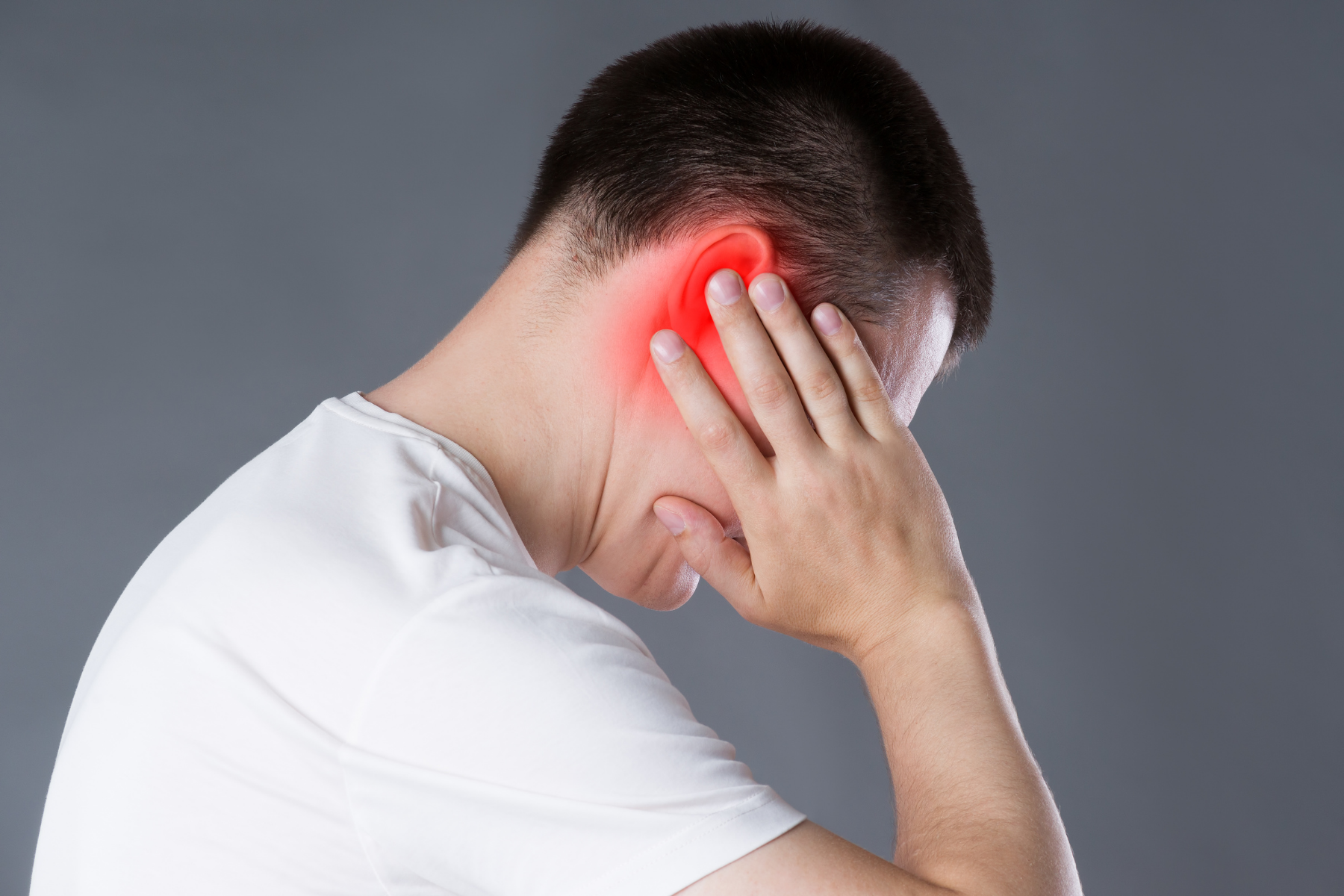 Person in white shirt holding ear showing red inflammation, depicting ear cartilage pain common in relapsing polychondritis