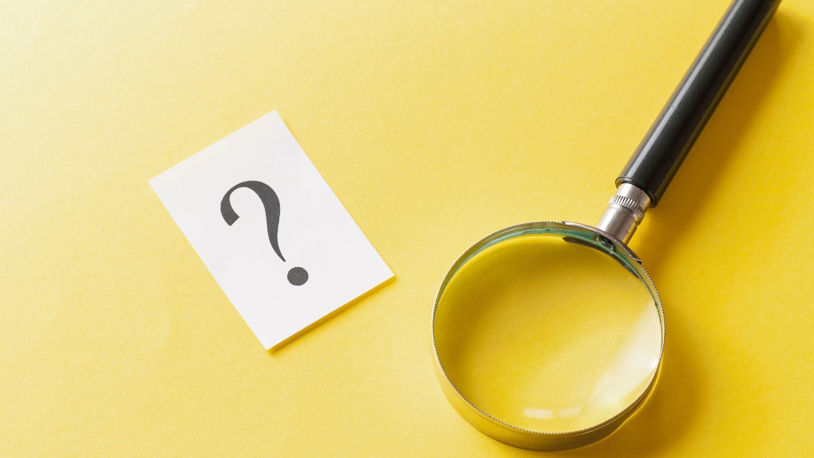 A magnifying glass and a paper with a question mark on a yellow background