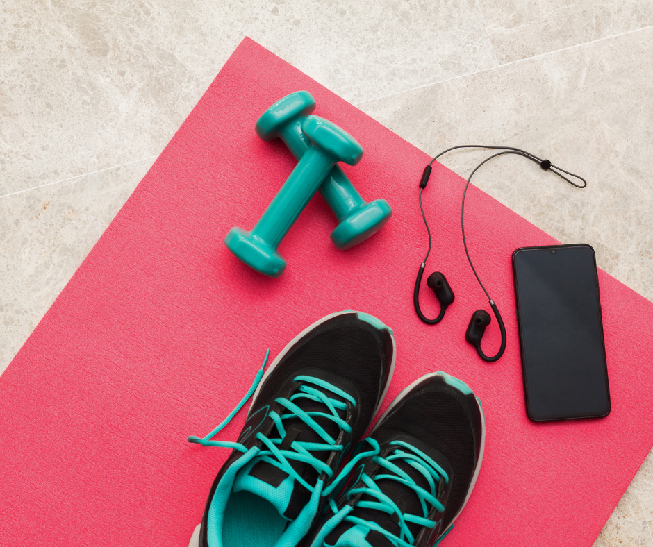 Exercise equipment on pink yoga mat: teal dumbbells, black and turquoise sneakers, phone & earbuds