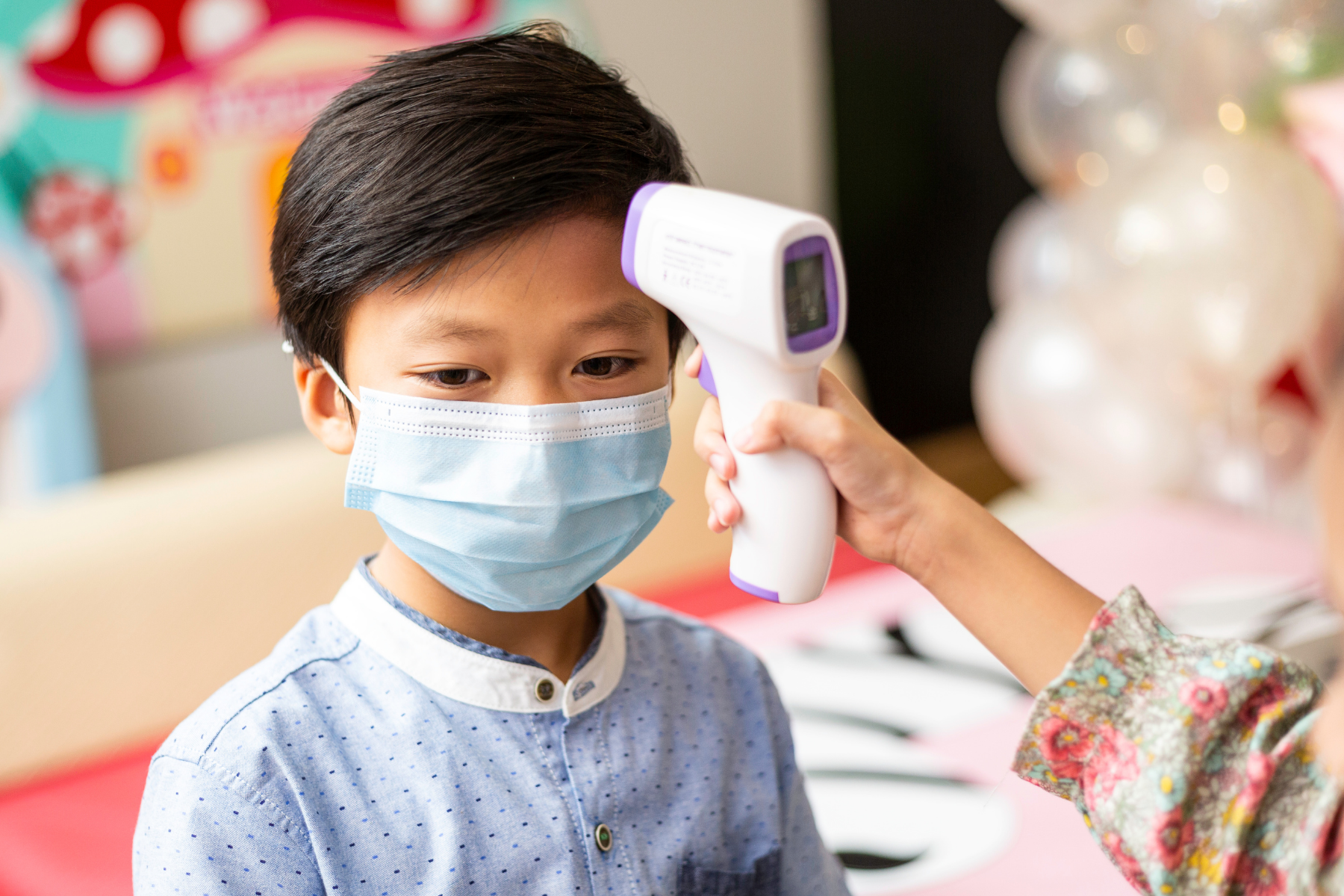 Child with mask having temperature checked, as fever and illness monitoring is important for kids with Juvenile Idiopathic Arthritis