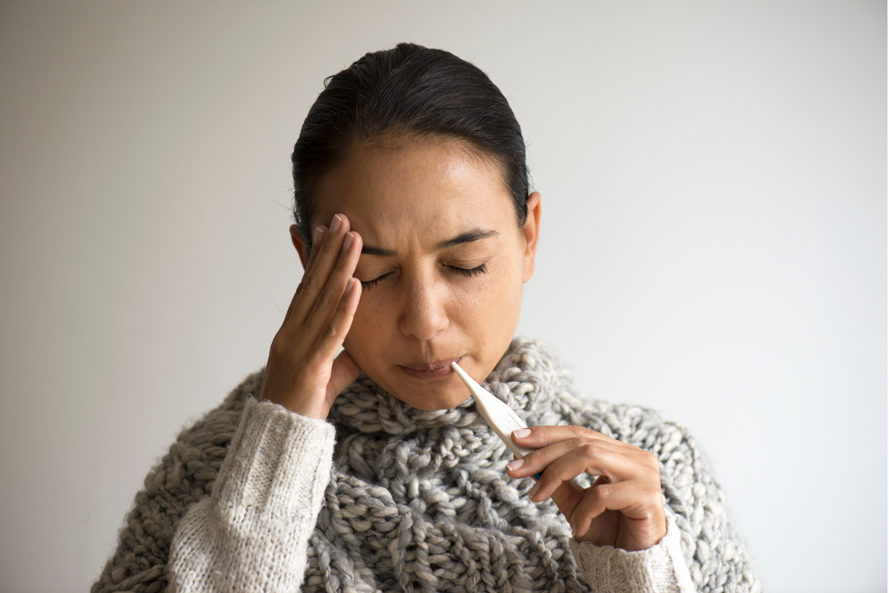 Woman checking for fever during a Familial Mediterranean Fever attack, showing typical symptoms of fever and headache