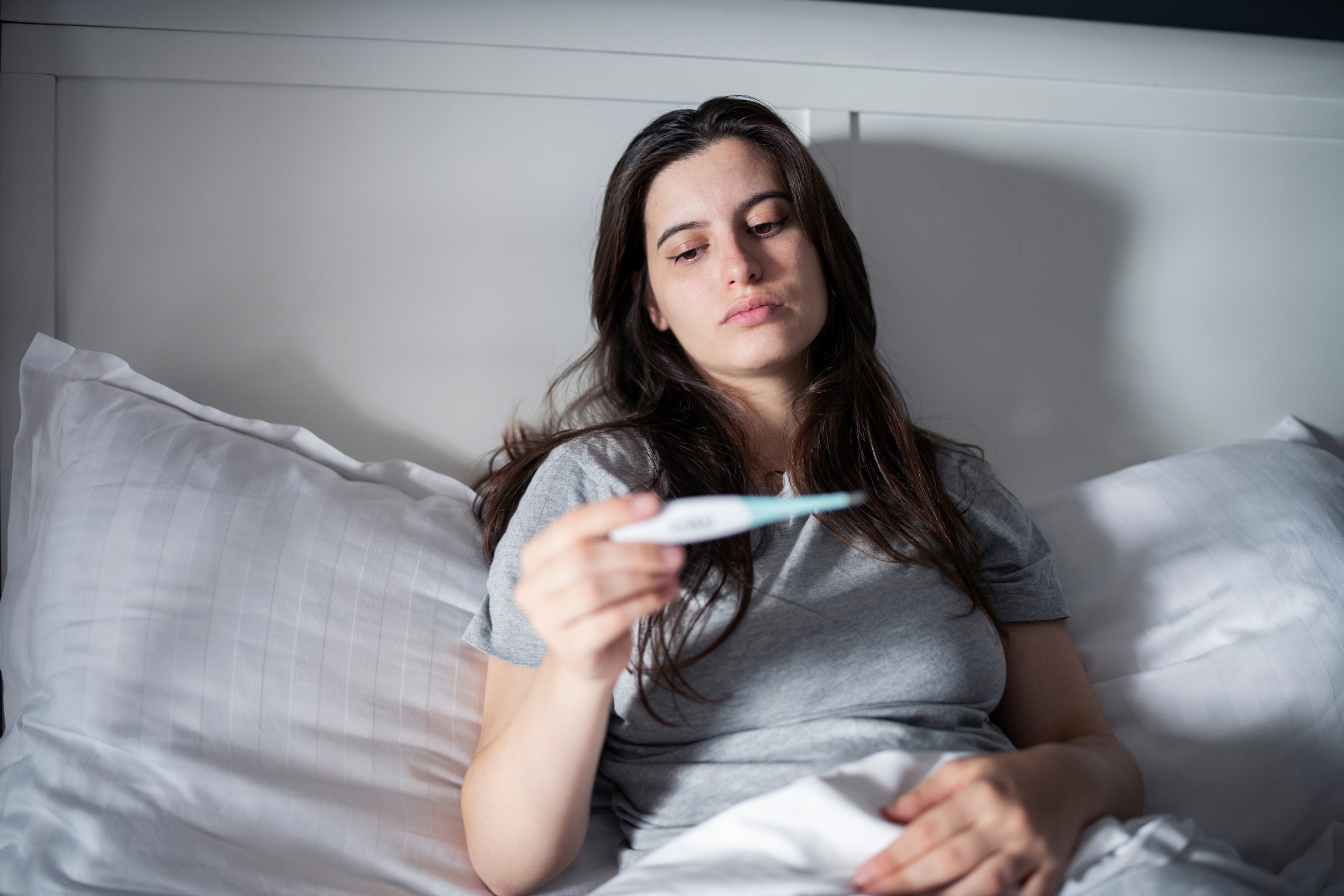 Woman in bed checking temperature during a HIDS fever attack, a characteristic recurring symptom of the condition