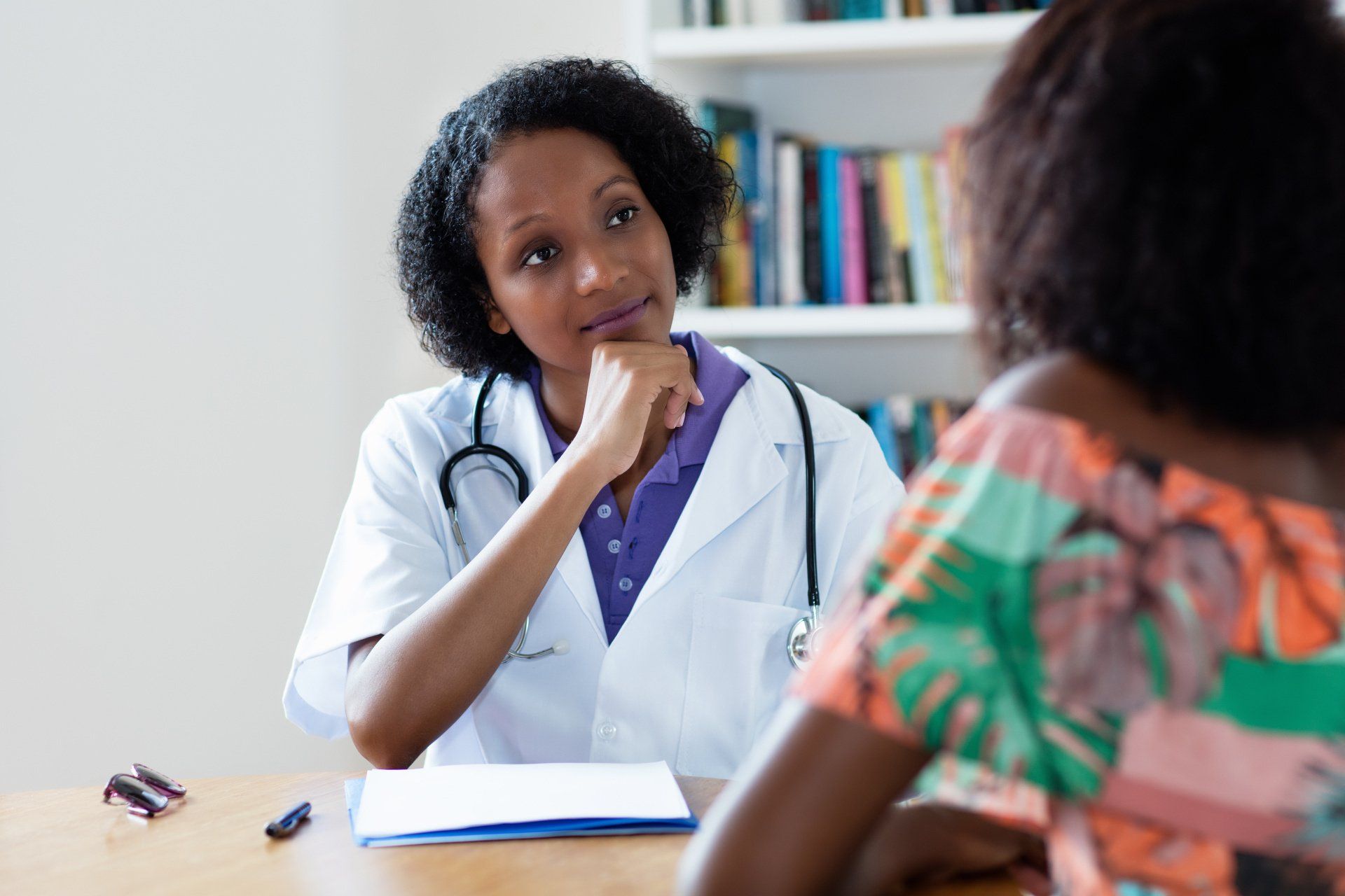 A scene showing a medical professional in a white coat and stethoscope listening attentively to someone seated across from them, representing clinical trials decision-making assistance