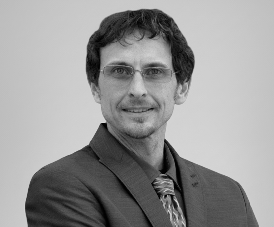 Man with glasses, wearing a suit, smiling.