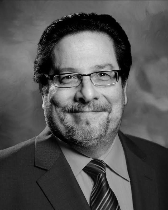 Ami Patel: Woman with long dark hair wearing professional attire and necklace, with a confident smile