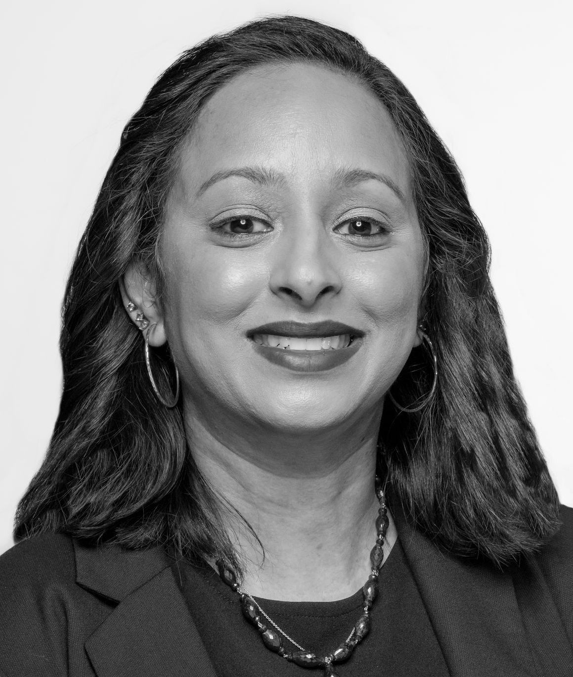 Ami Patel: Woman with long dark hair wearing professional attire and necklace, with a confident smile