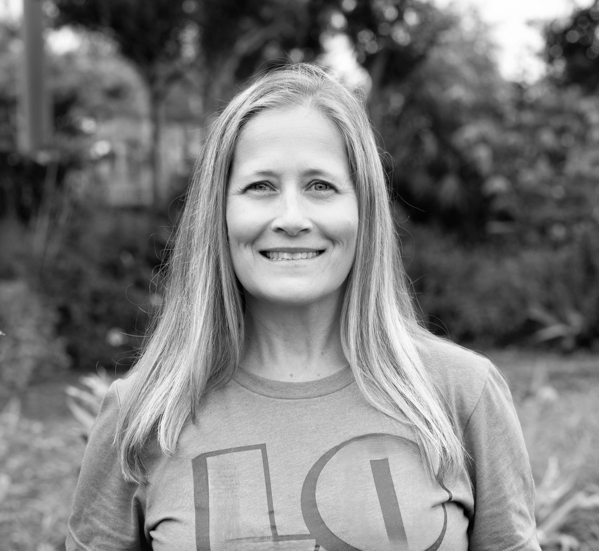 Woman with long hair, smiling, wearing a t-shirt with “love” on it, outdoors.