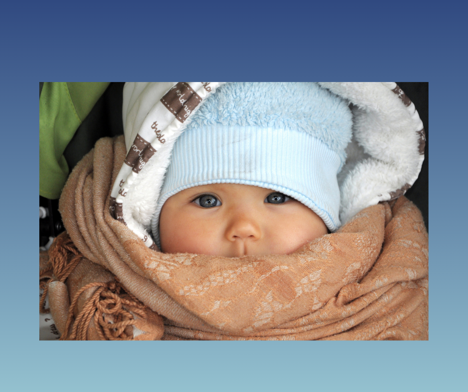 Baby wearing light blue winter hat and brown scarf, bundled up warmly.