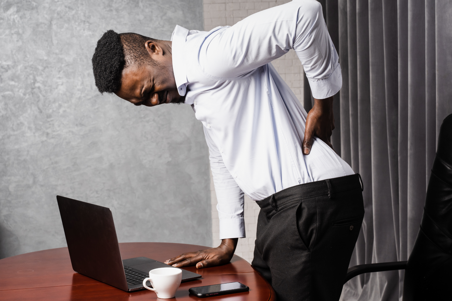 Business professional holds lower back and winces, demonstrating inflammation, one of the axial spondyloarthritis symptoms.