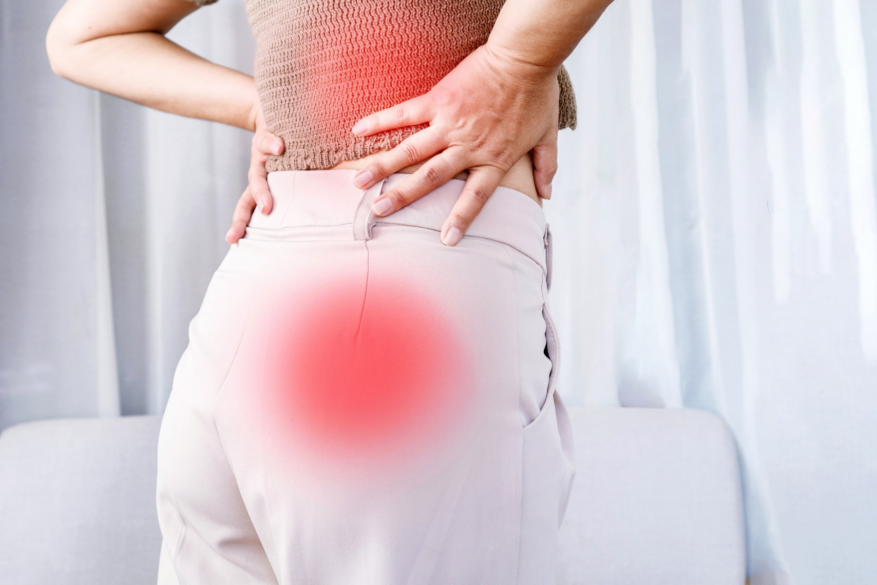 Medium shot. Person holds lower back. Two red spots at the lower back and sacroiliac joint indicate pain in these areas, symptoms that can help with diagnosing axial spondyloarthritis.