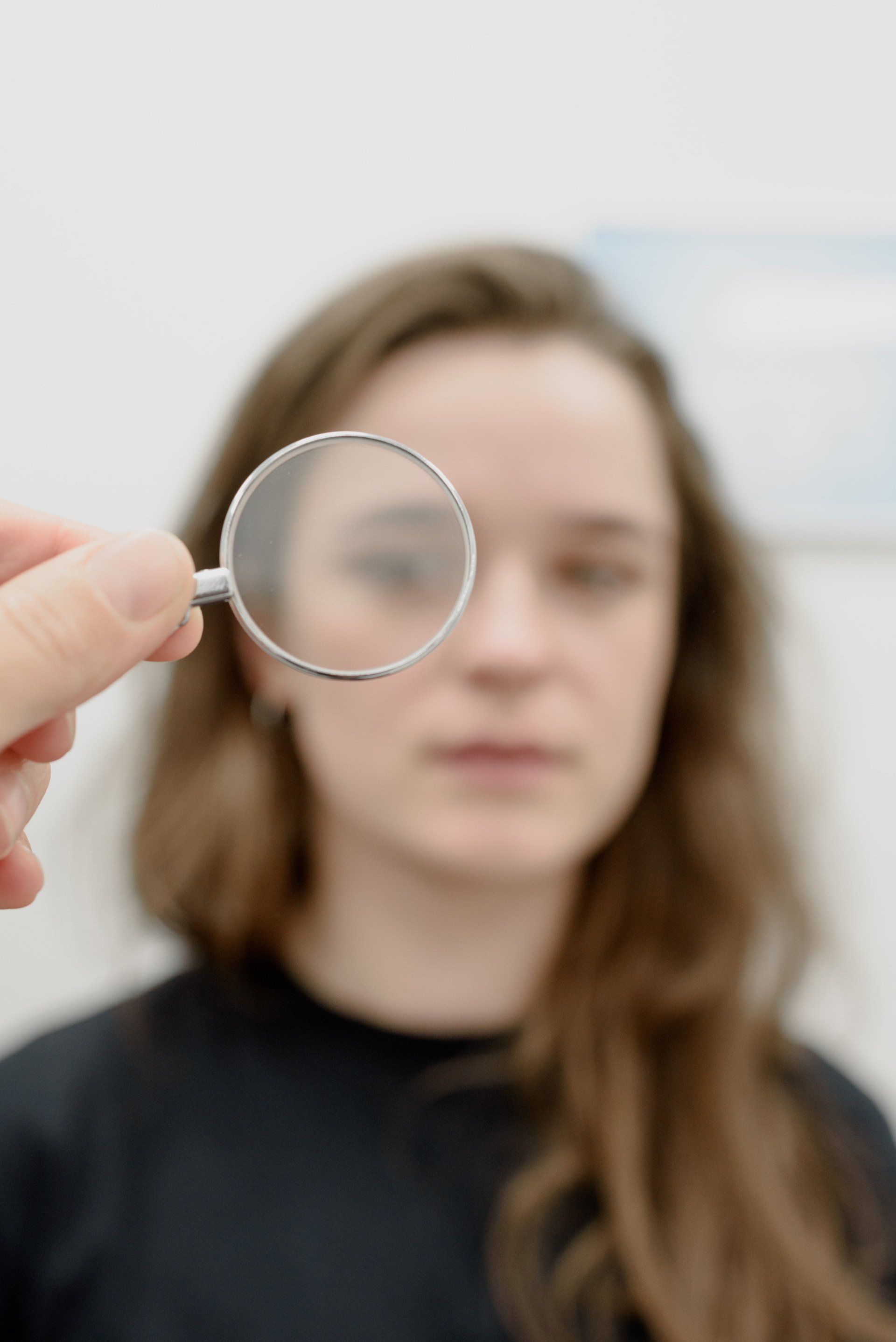 Background of woman with nervous expression is out of focus, in the foreground an in focus magnifying glass placed in front of her right eye.