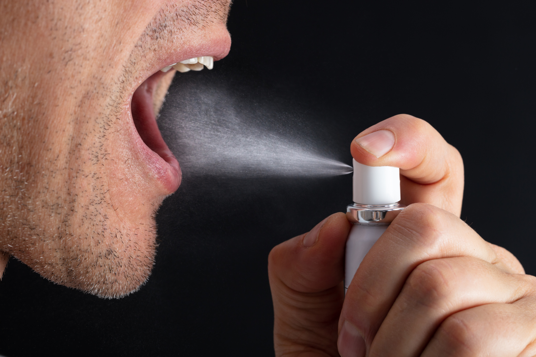 Close-up profile of a man using oral spray demonstrating treatment for dry mouth, one of the Sjögren's symptoms