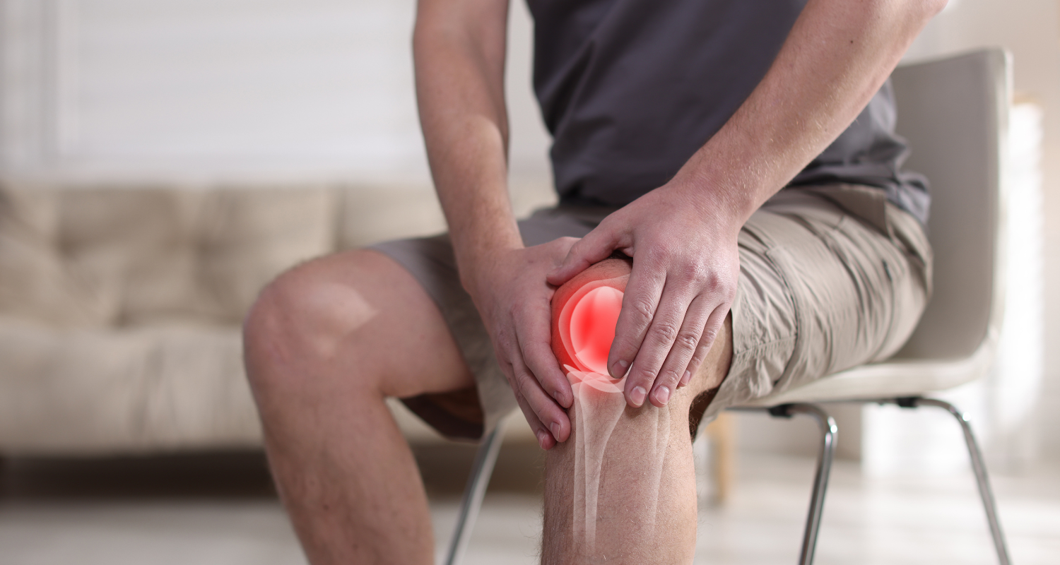 Person seated on a chair, clutching a glowing red knee in pain