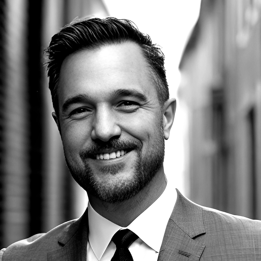 Ray Patnaude: Man with short dark hair and facial hair, wearing a suit and tie, with a professional smile