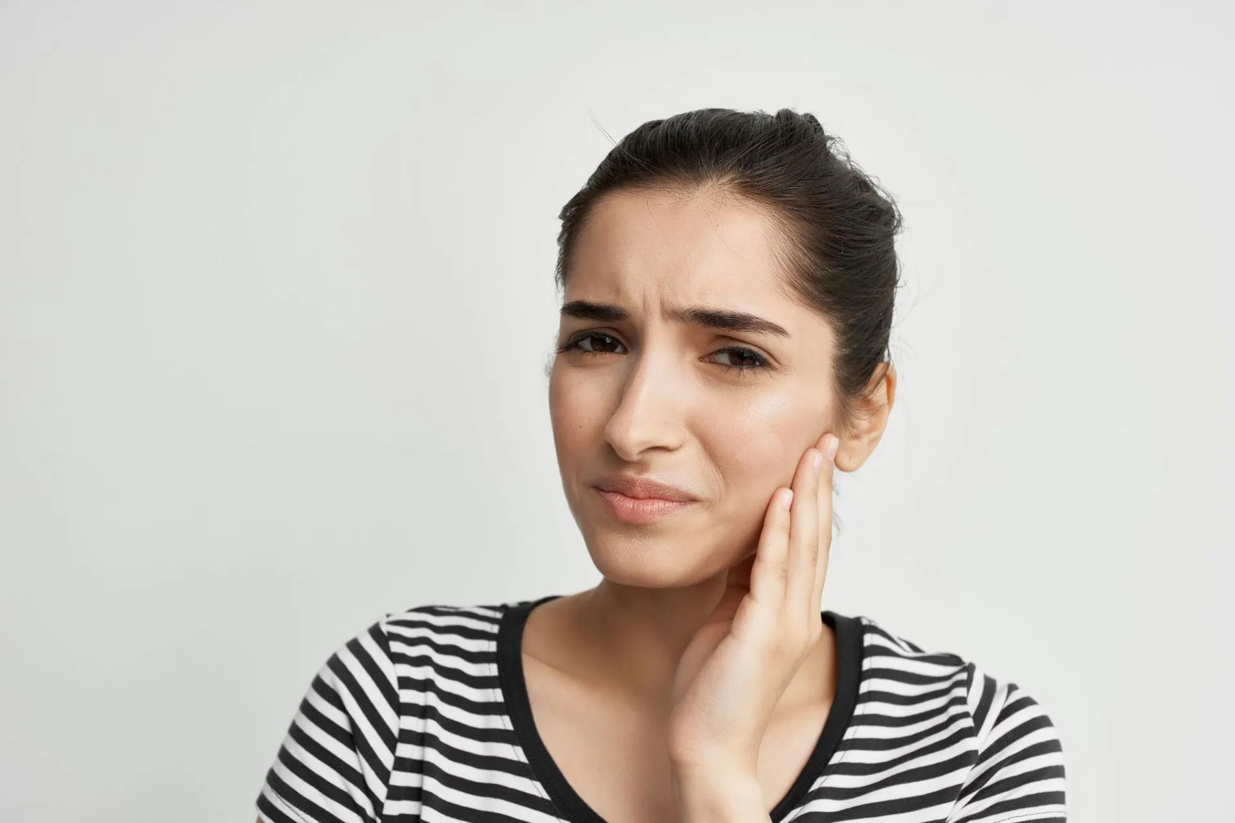 Woman in striped shirt touches her cheek showing discomfort from swollen salivary glands, one of the common Sjögren's symptoms.