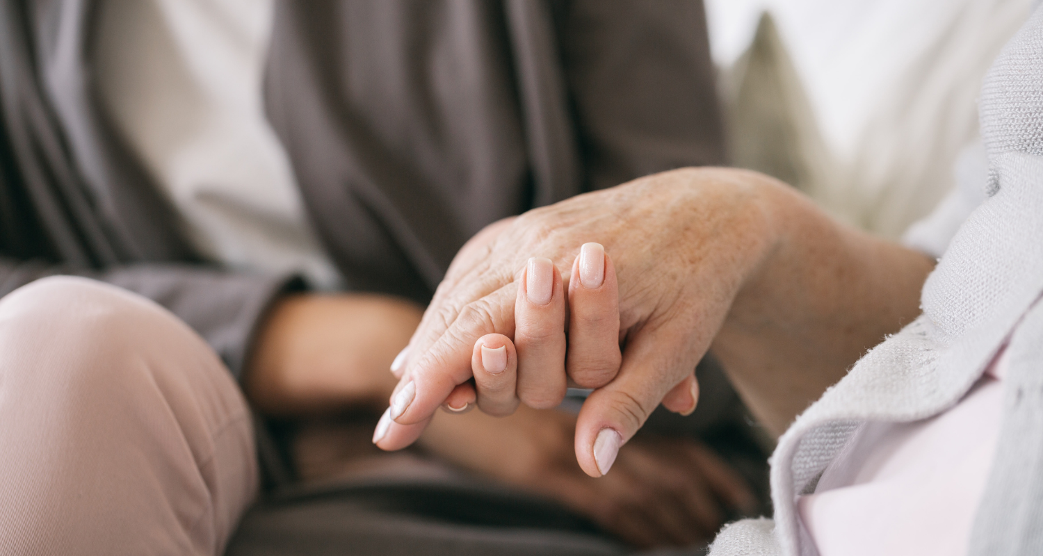 Two elderly hands, one resting on the other, showing a gesture of comfort and support.