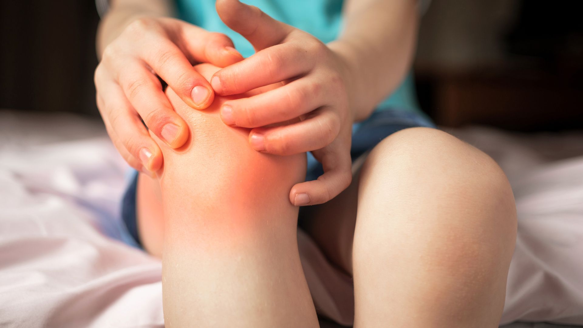 Child holding knee with visible redness, likely indicating pain.