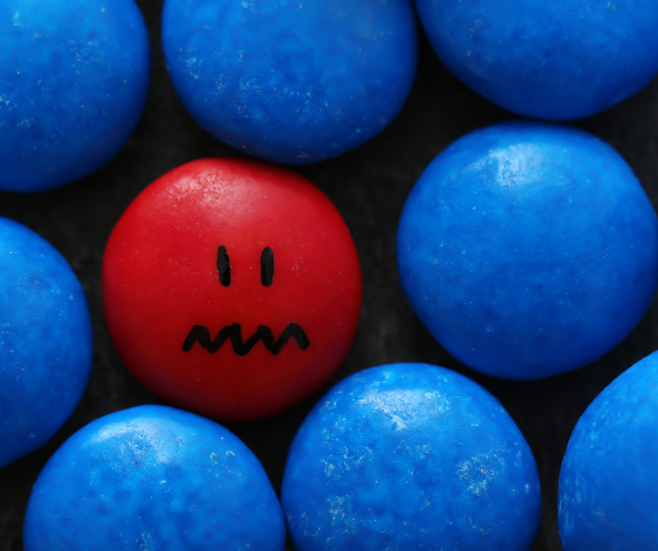 Blue candies with one red that has a worried face drawn on it