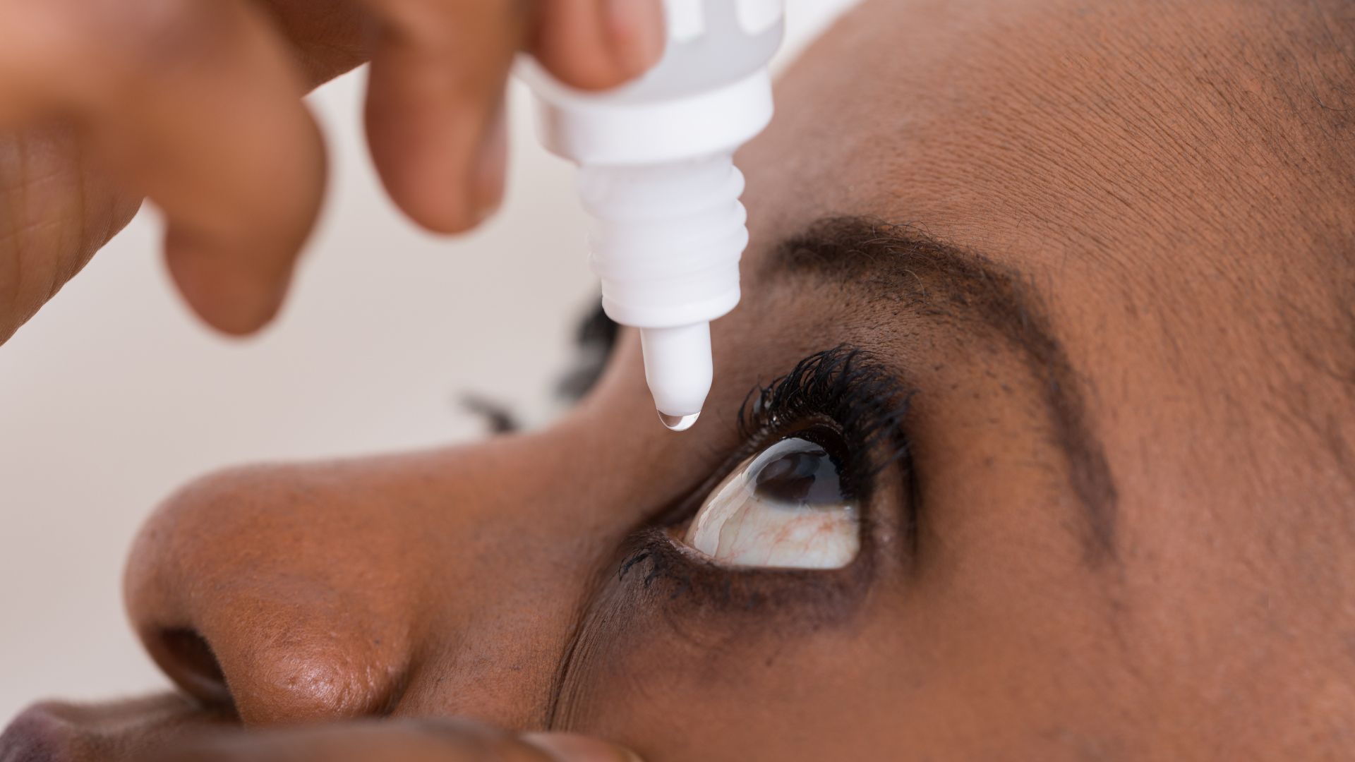 Person applying eye drops to their eye, indoors.