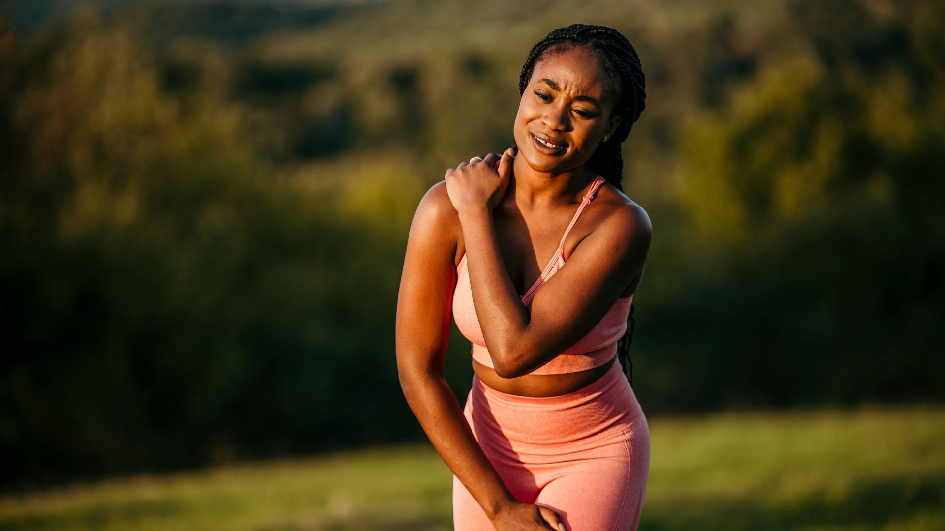 Woman in activewear clutches her shoulder in pain outdoors.
