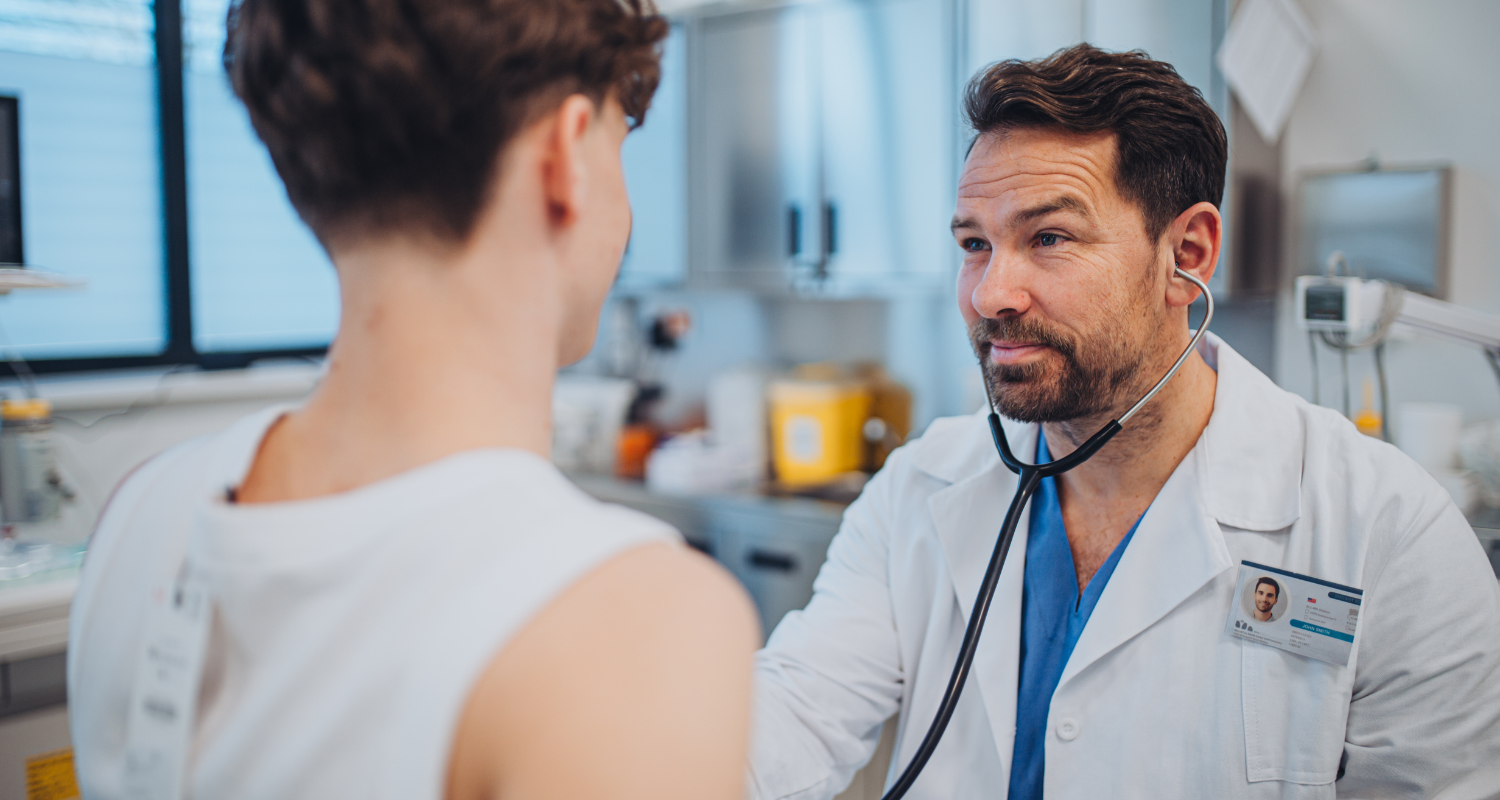 Doctor listens to patient's back with stethoscope in medical examination room.